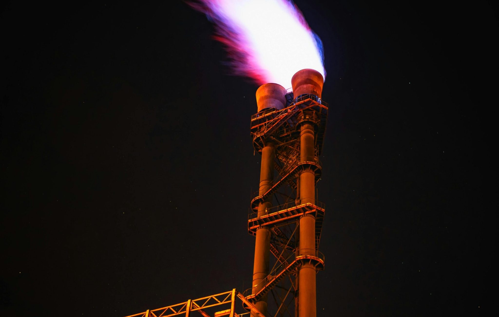 Dramatic night photo of gas flare on industrial facility emitting a powerful flame.